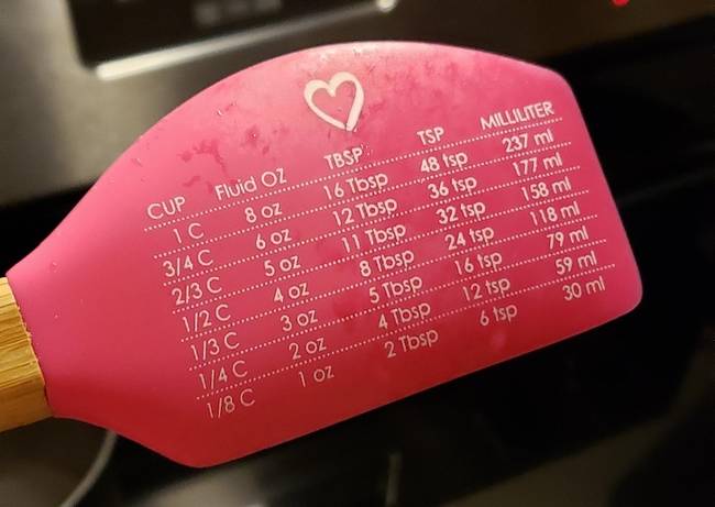 Egy spatula, amely tartalmazza a különböző főzéshez használt mértékegységek átváltási táblázatát.