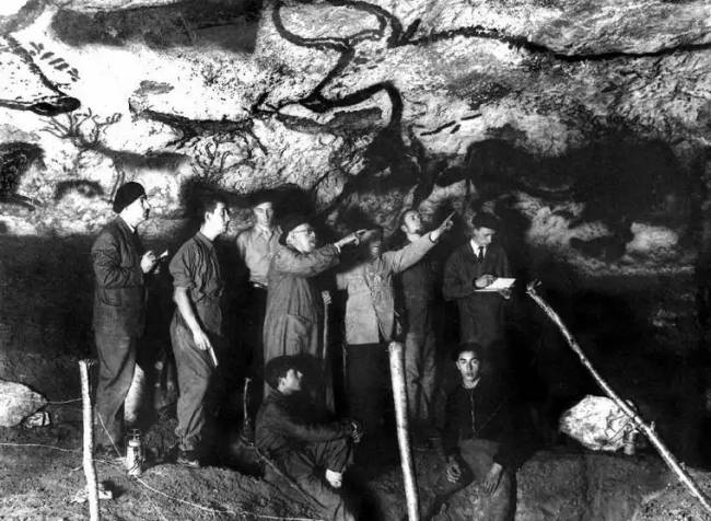 Tinédzserek és néhány kutató sziklaművészetet tanulmányoznak a Lascaux-barlangban.
