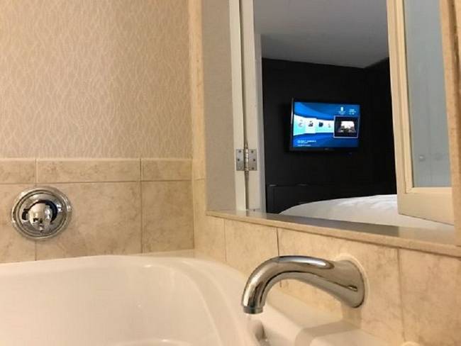 Ebben a hotelszobában egy kis ablakon keresztül a fürdőből is nézhető a tévé.