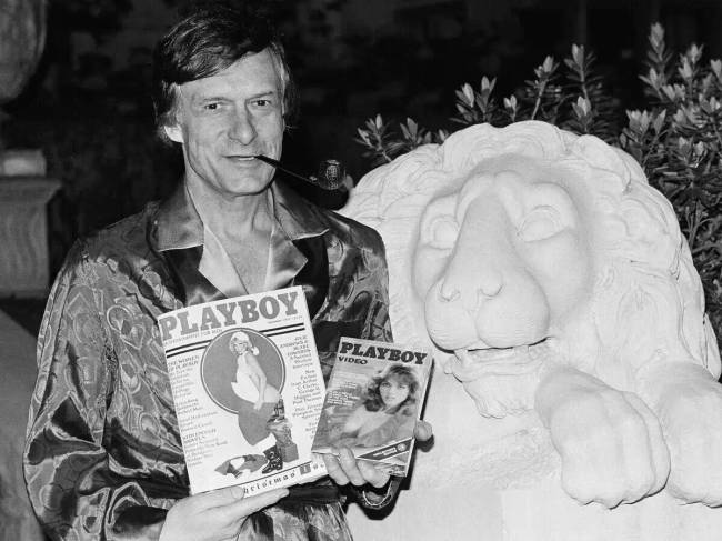 Hugh Hefner egy Playboy magazint és egy Playboy Channel-ről származó videokazettát tart a kezében egy interjú során a holmby hills-i Playboy-kúriában. 1982. november 29.
