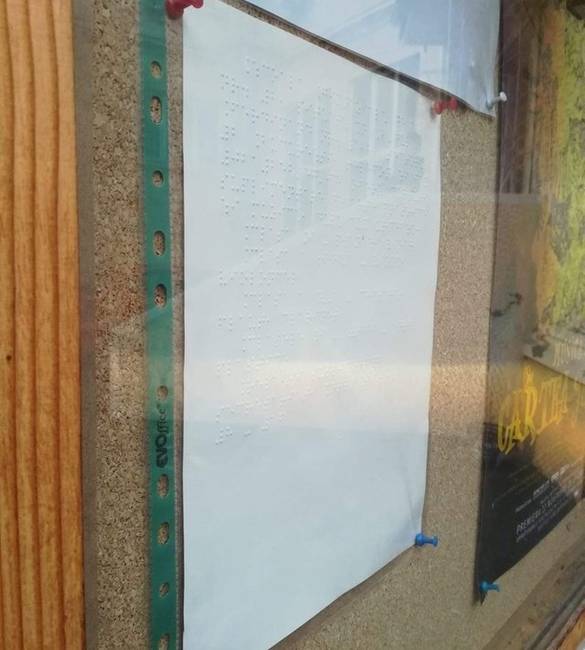 Braille-írás egy plexi mögött, irattartó tasakban.